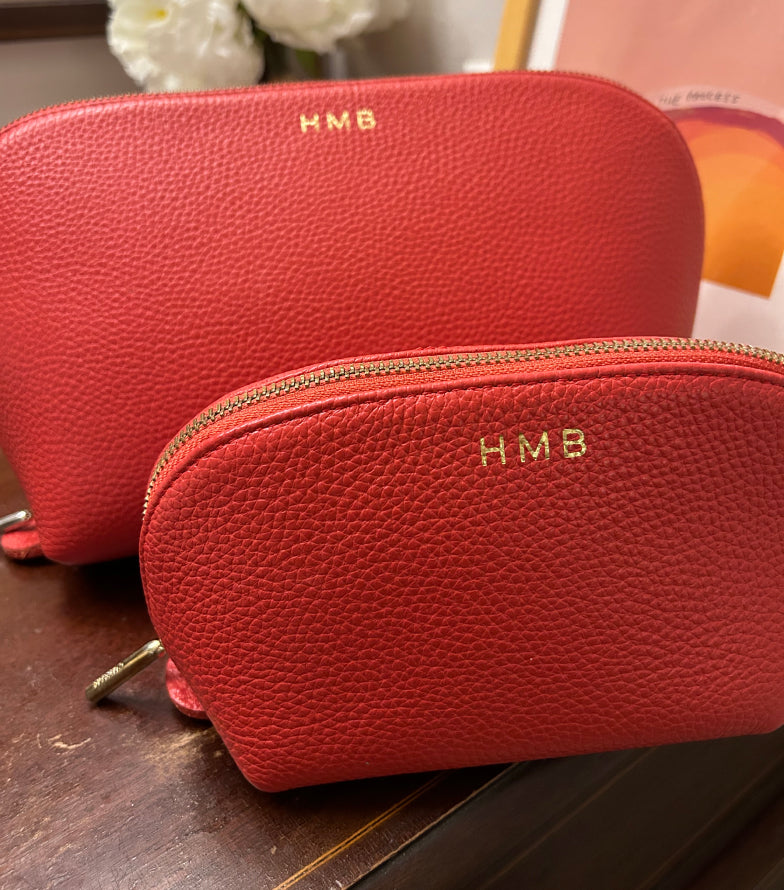 Two small zippered pouches with monogram initials HMB, positioned on a wooden surface.