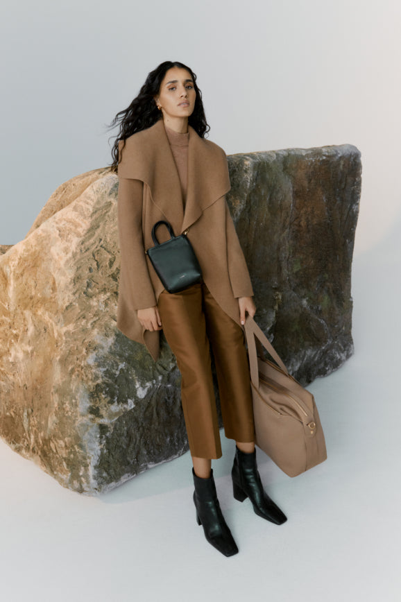 Woman standing next to a large rock holding a bag and a purse.