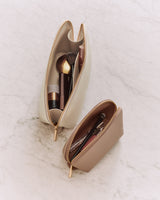 Two makeup bags with brushes and cosmetics on a marble surface.
