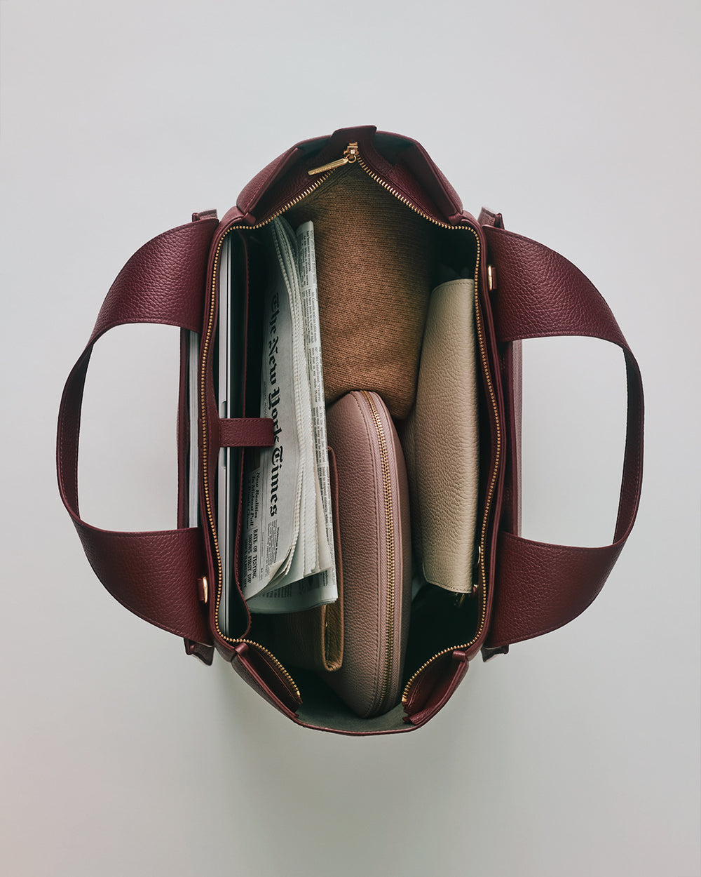 Mila Satchel Top view of an open travel bag containing a newspaper and a few pouches.