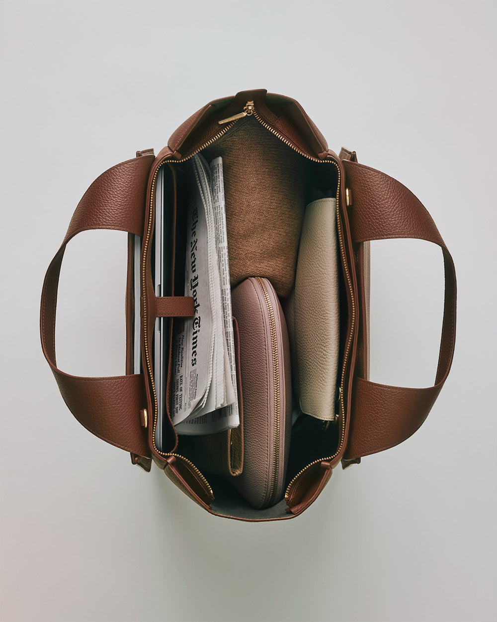 Mila Satchel Open travel bag with contents including a newspaper, and various neatly arranged items.