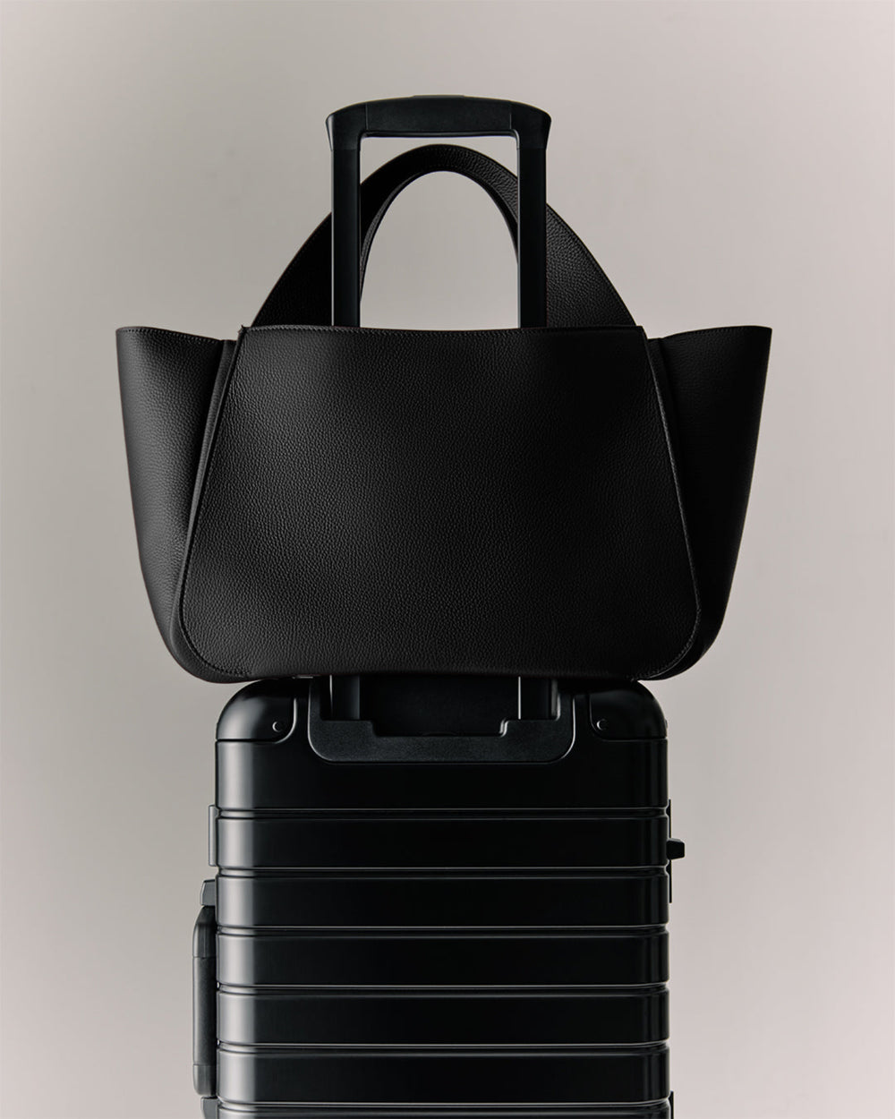 Mila Satchel A travel bag placed on top of a wheeled suitcase.