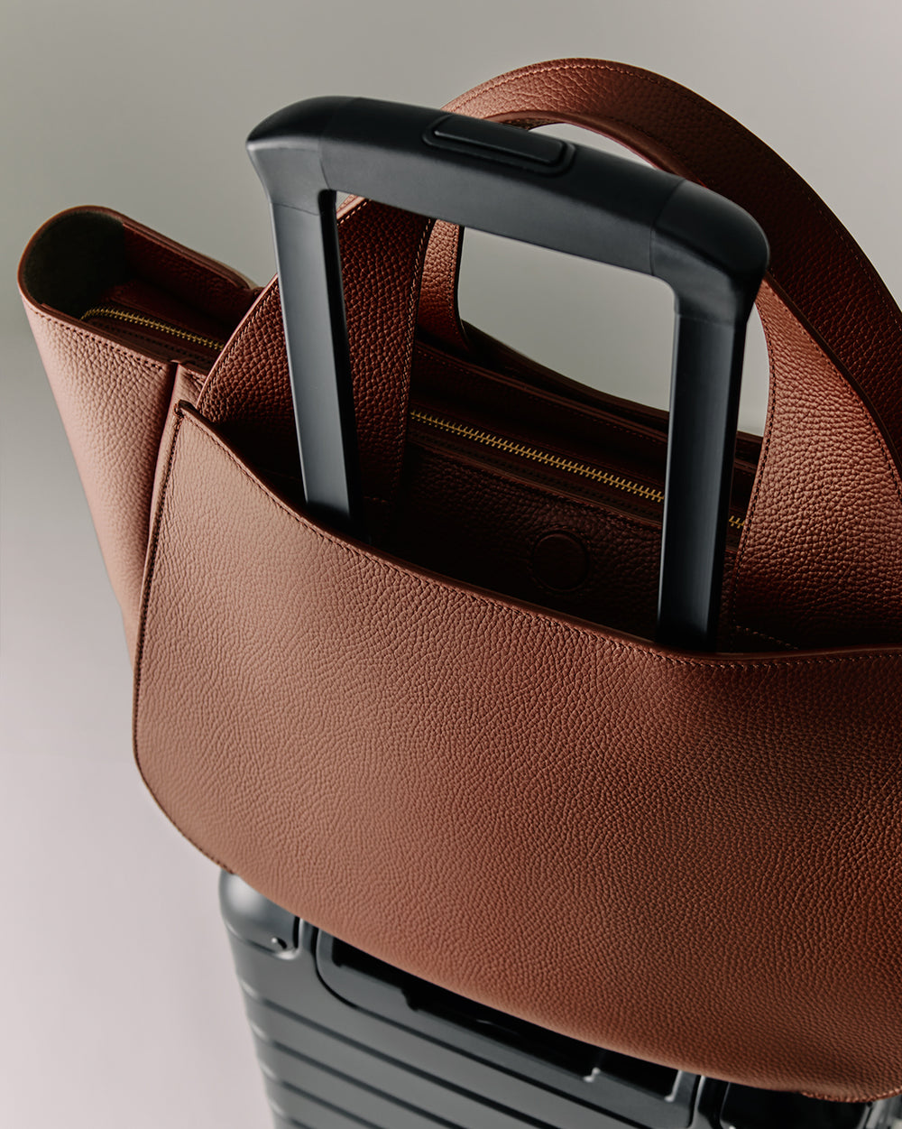 Mila Satchel Large handbag attached to the retractable handle of a suitcase.