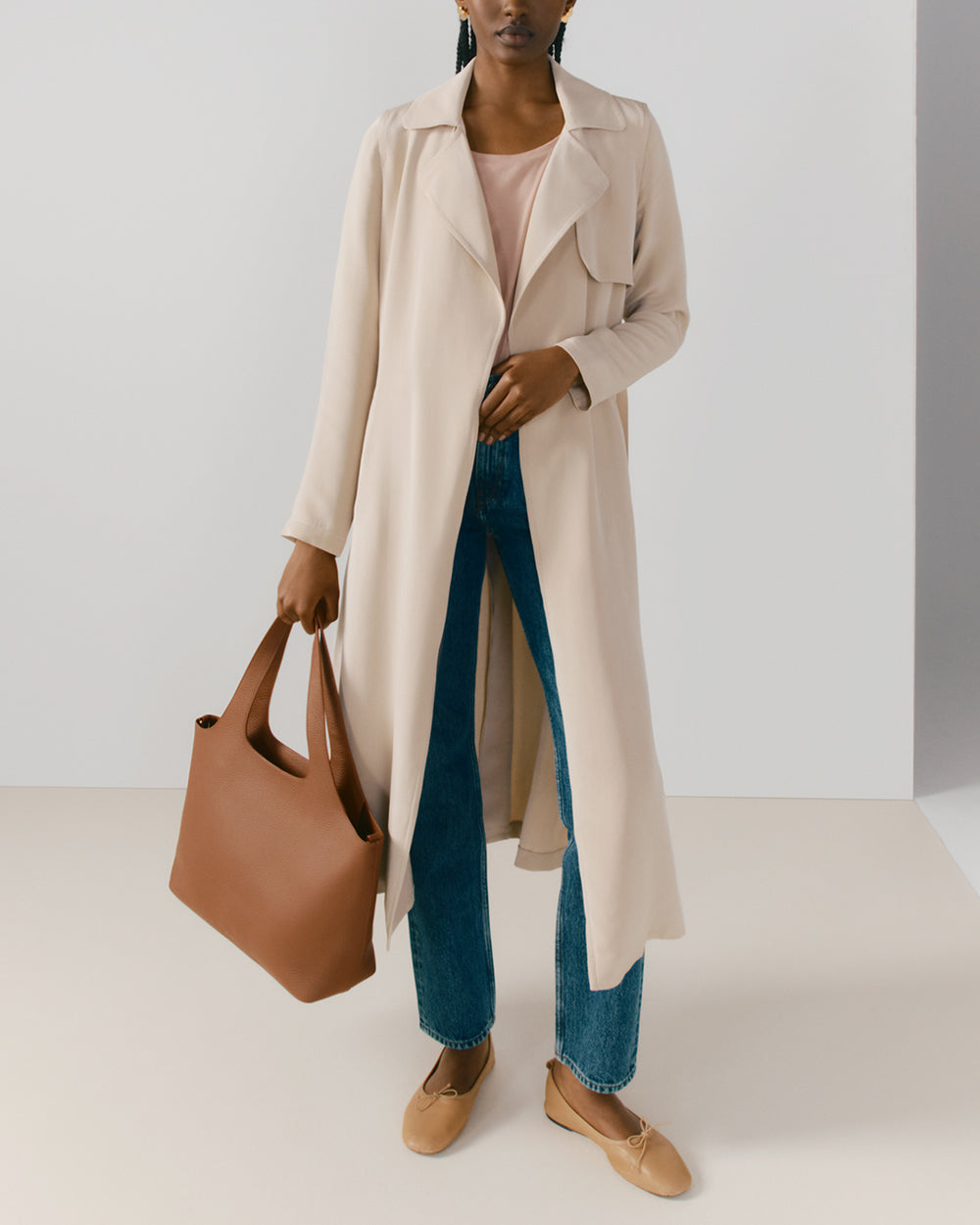 Person wearing long coat, jeans, holding a large bag, and wearing flats.