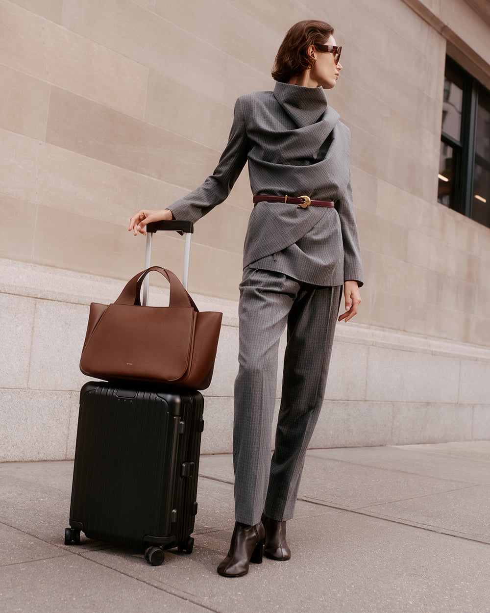 Mila Satchel Person in suit standing with travel bag on luggage and wearing sunglasses.