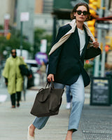 Person in a blazer and jeans carrying a large tote bag on a city street.
