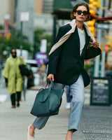 Person in a blazer and jeans carrying a large tote bag on a city street.