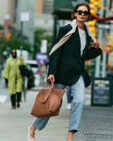 Person in a blazer and jeans carrying a large tote bag on a city street.