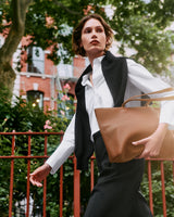 Person walking with a large handbag outdoors near a fence and trees.