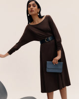 Person in dress with belt holding clutch bag, leaning slightly with arm extended.