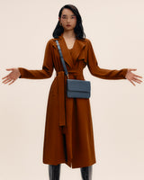 Person wearing a long coat with a small crossbody bag and knee-high boots.