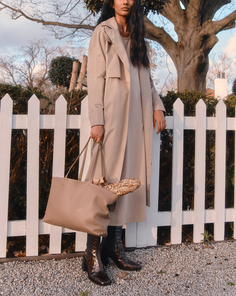 Small Easy Tote Woman in long coat holding tote bag standing by a white picket fence.