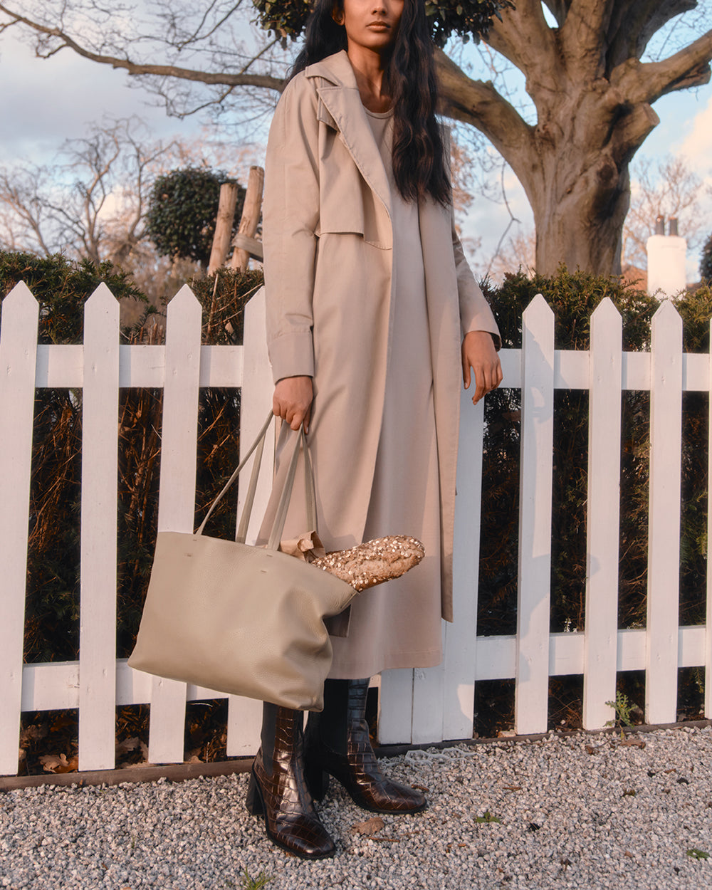 Small Easy Tote Woman in long coat holding tote bag standing by a white picket fence.