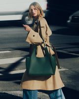 Person in a coat walking across the street carrying a large handbag.