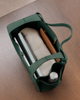 Open bag with a sweater, notebook, wallet, and water bottle inside on a wooden surface.