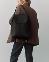 Person holding a backpack over their shoulder, wearing a blazer and jeans.