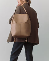 Person holding a backpack over their shoulder, wearing a blazer and jeans.