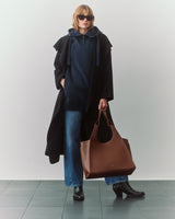 Person wearing a cape, hoodie, jeans, boots, with a large tote bag and sunglasses.