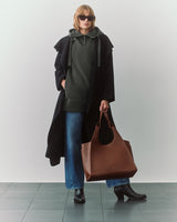 Person wearing a cape and holding a large tote bag.