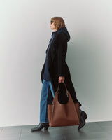 Person in a cape and jeans carrying a large bag, walking indoors.