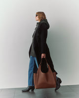 Person in cape carrying large bag, wearing sunglasses and jeans, walking indoors.