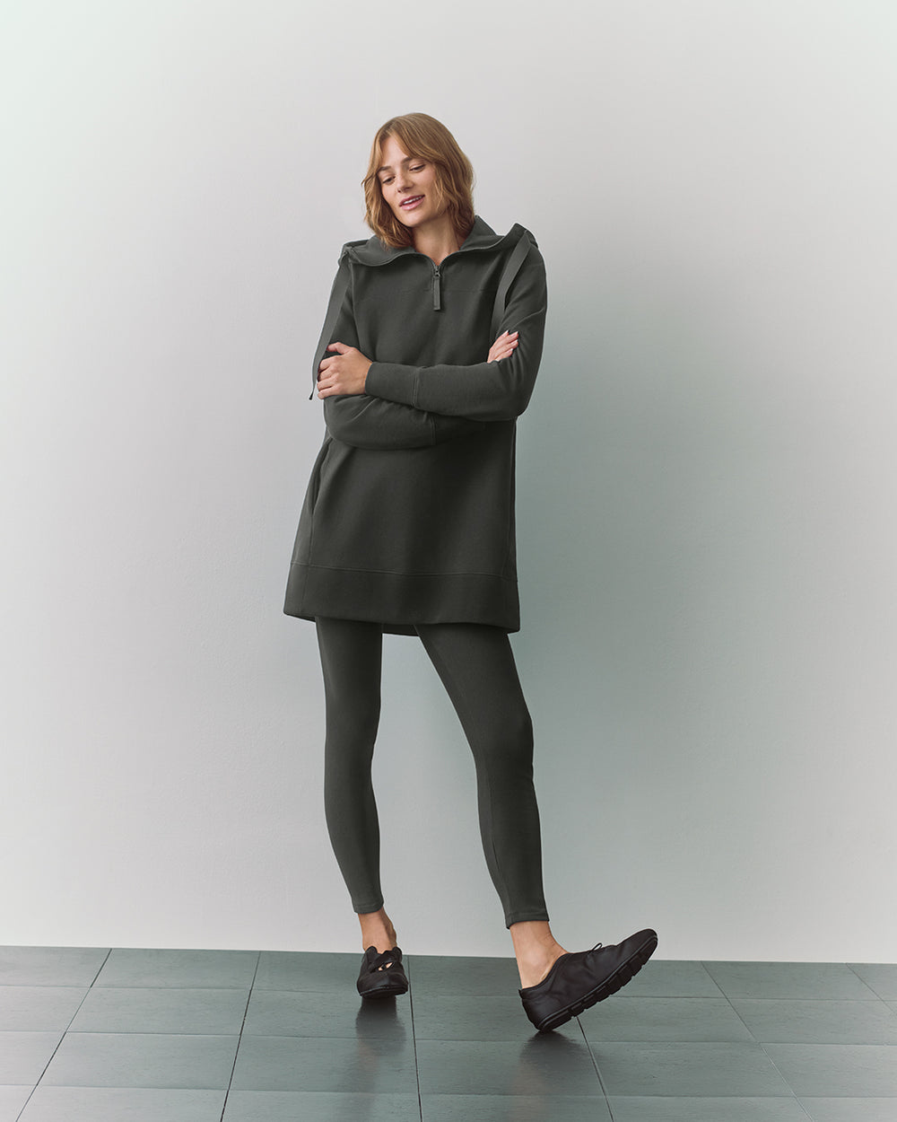 Person wearing tunic and leggings with arms crossed, standing on tiled floor.