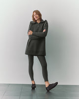 Person wearing tunic and leggings with arms crossed, standing on tiled floor.