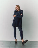 Person in long-sleeve shirt and leggings, wearing shoes, standing with arms crossed.