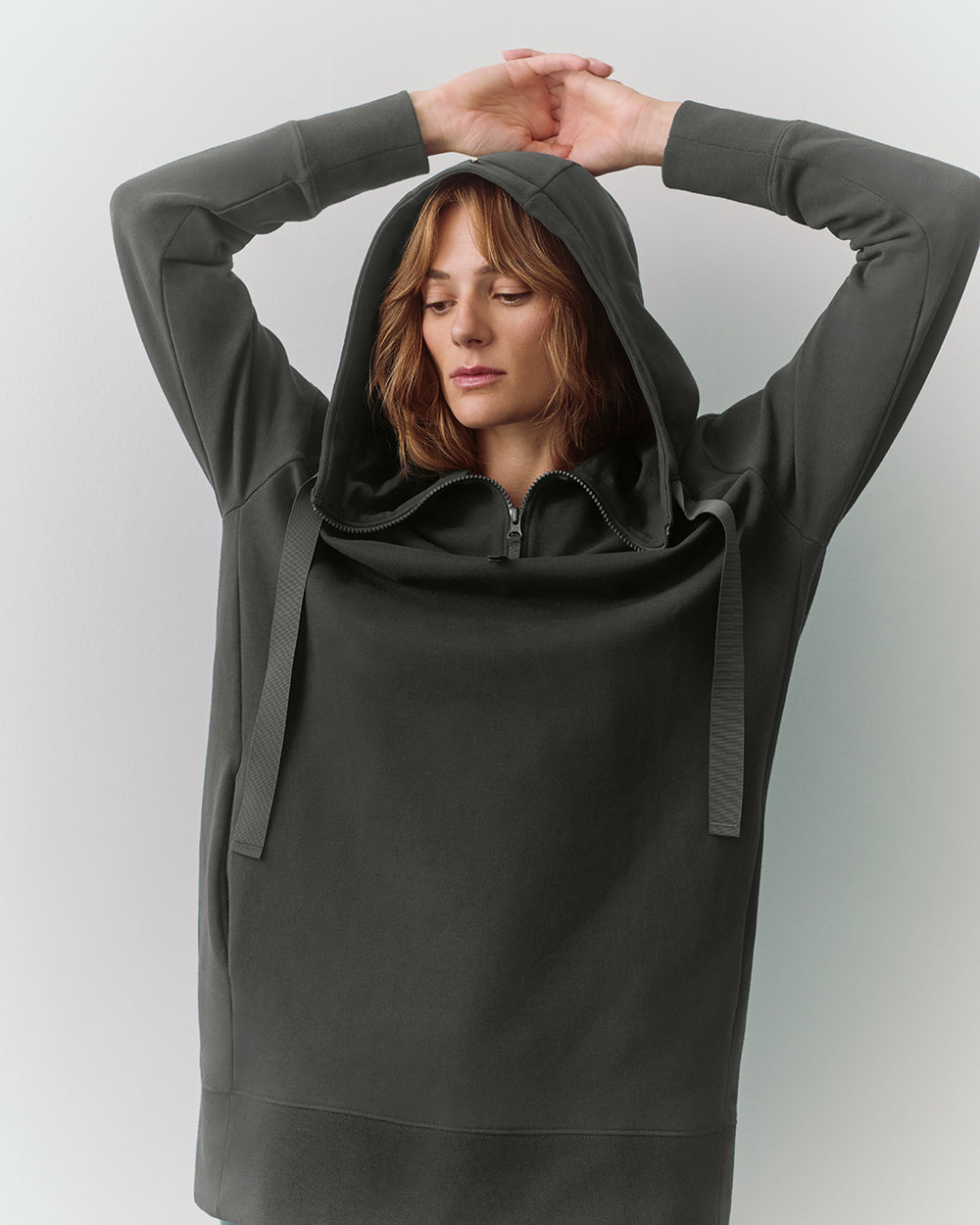 Person wearing a hooded sweatshirt with arms raised overhead.