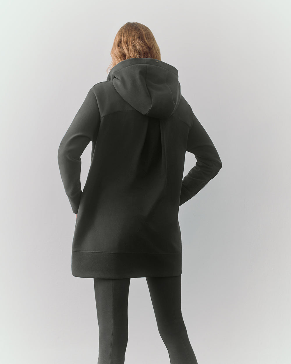 Person wearing hooded sweater and pants, facing away.