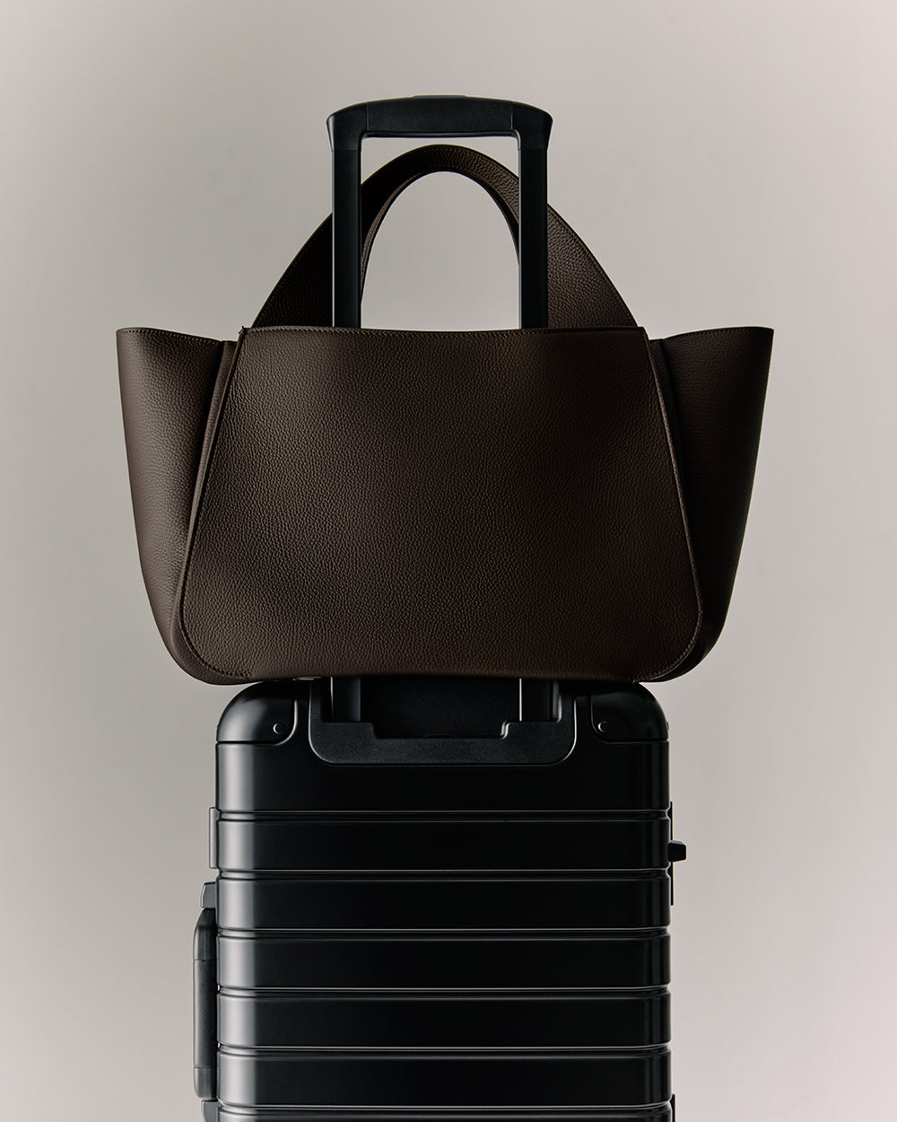 Mila Satchel Tote bag resting on a wheeled suitcase handle.