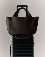 Tote bag resting on a wheeled suitcase handle.