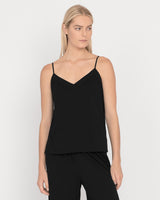 Woman standing in a sleeveless top and pants looking to the side.