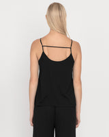 Woman standing with her back facing the camera wearing a tank top with crisscross straps.