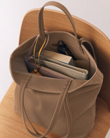 Tote bag on chair, filled with books, notebook, folder, and sunglasses.