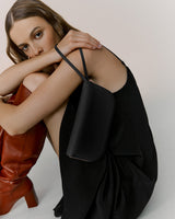 Woman sitting with a purse, leaning forward and holding her arm.