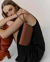 Person sitting with a shoulder bag, wearing a dress and high boots.