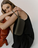 Woman sitting and holding a shoulder bag, looking at the camera.