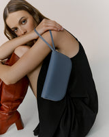 Woman sitting and holding a handbag on her shoulder.