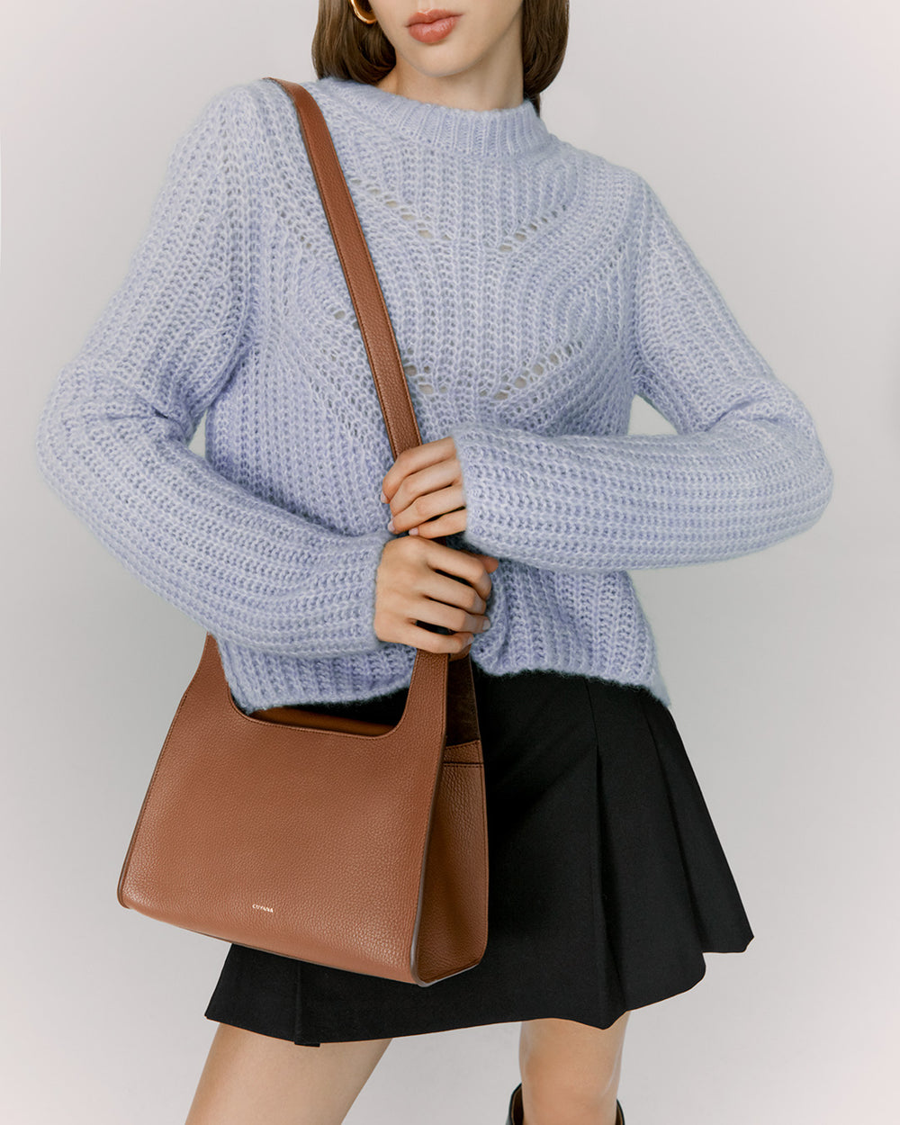 Woman in a sweater and skirt holding a shoulder bag.