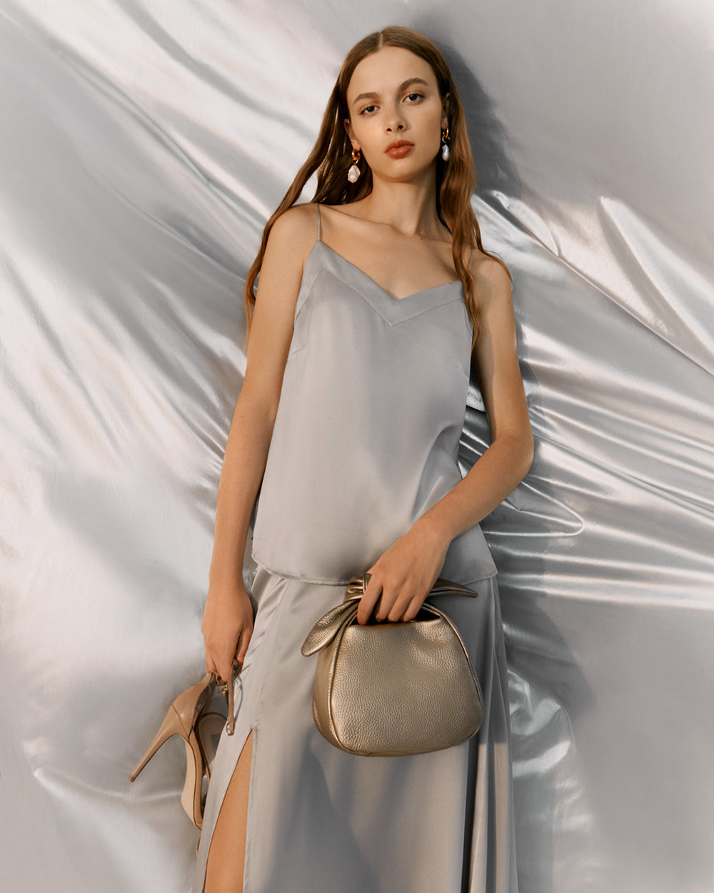 Woman standing with a handbag and holding a pair of shoes.