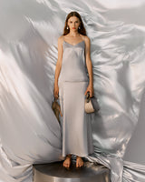 Woman standing on a platform with a metallic backdrop, holding a handbag.