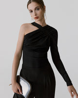 Woman posing in an asymmetric top, holding a clutch.