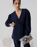 Woman standing and holding a clutch with one hand on her hip.