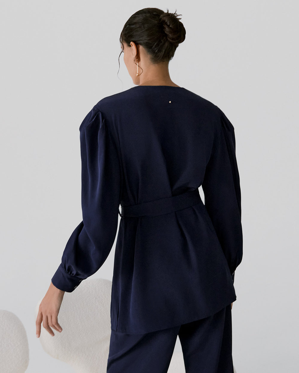 Woman in a belted top and pants standing in profile.