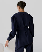 Woman in a belted top and pants standing in profile.