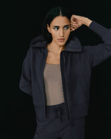 Woman in a hoodie and pants posing with her hand on her head.