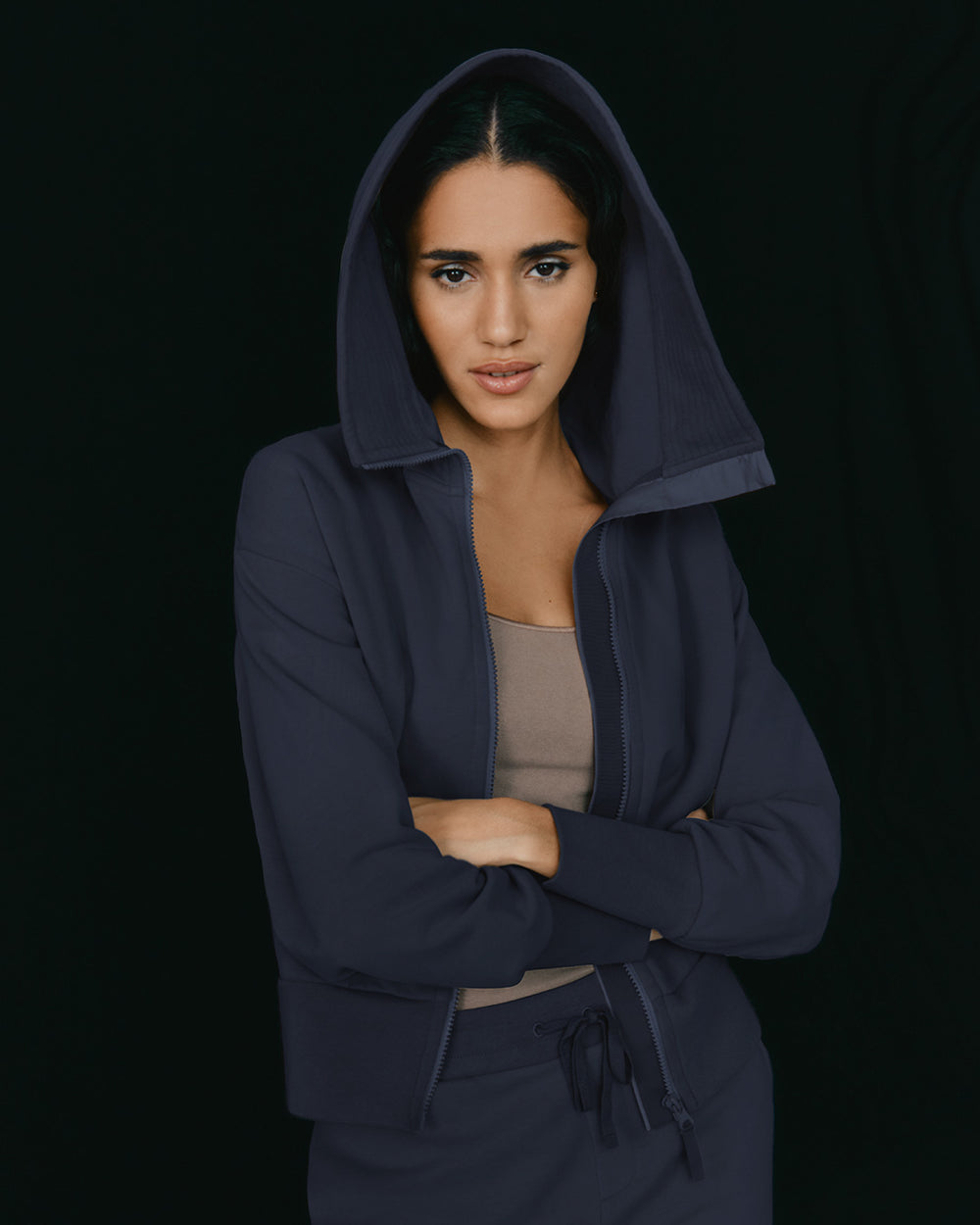 Woman in hooded jacket with arms crossed looking at camera