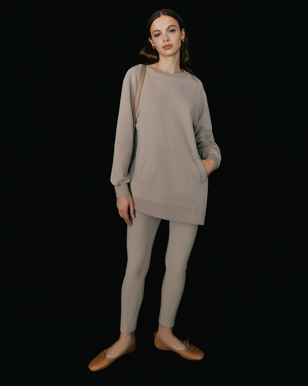 Woman standing in long sleeve top and leggings with hands by sides.
