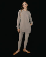 Woman standing in long sleeve top and leggings with hands by sides.
